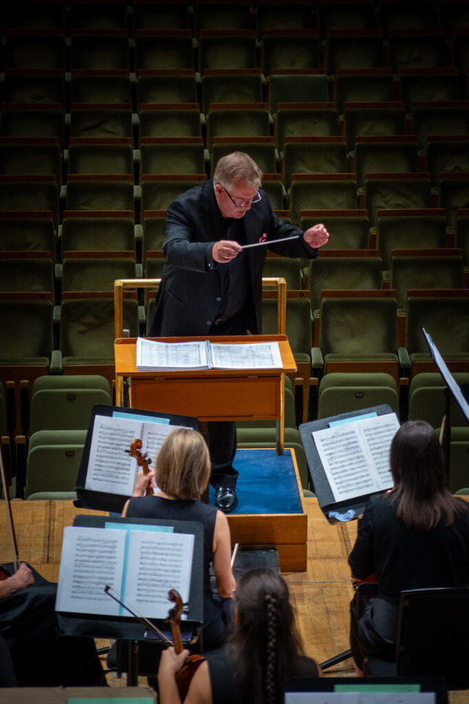 	Hibernian Orchestra conductor leading an orchestral rehearsal from the podium with string players and sheet music in the concert hall